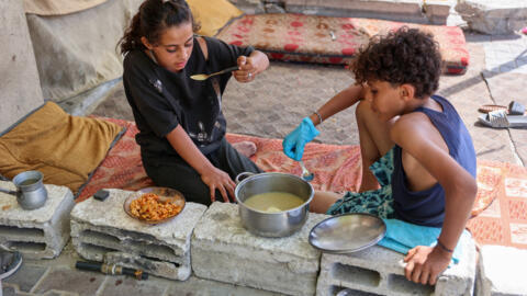 Niños desplazados comen un plato cocinado en su tienda de campaña en el dañado estadio Yarmouk de la ciudad de Gaza, el 14 de octubre de 2024.