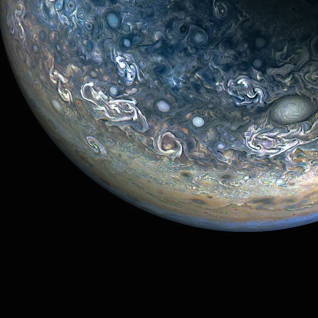 The blue-green outline of Jupiter against the blackness of space, with swirling clouds of white and blue on the planet's surface.