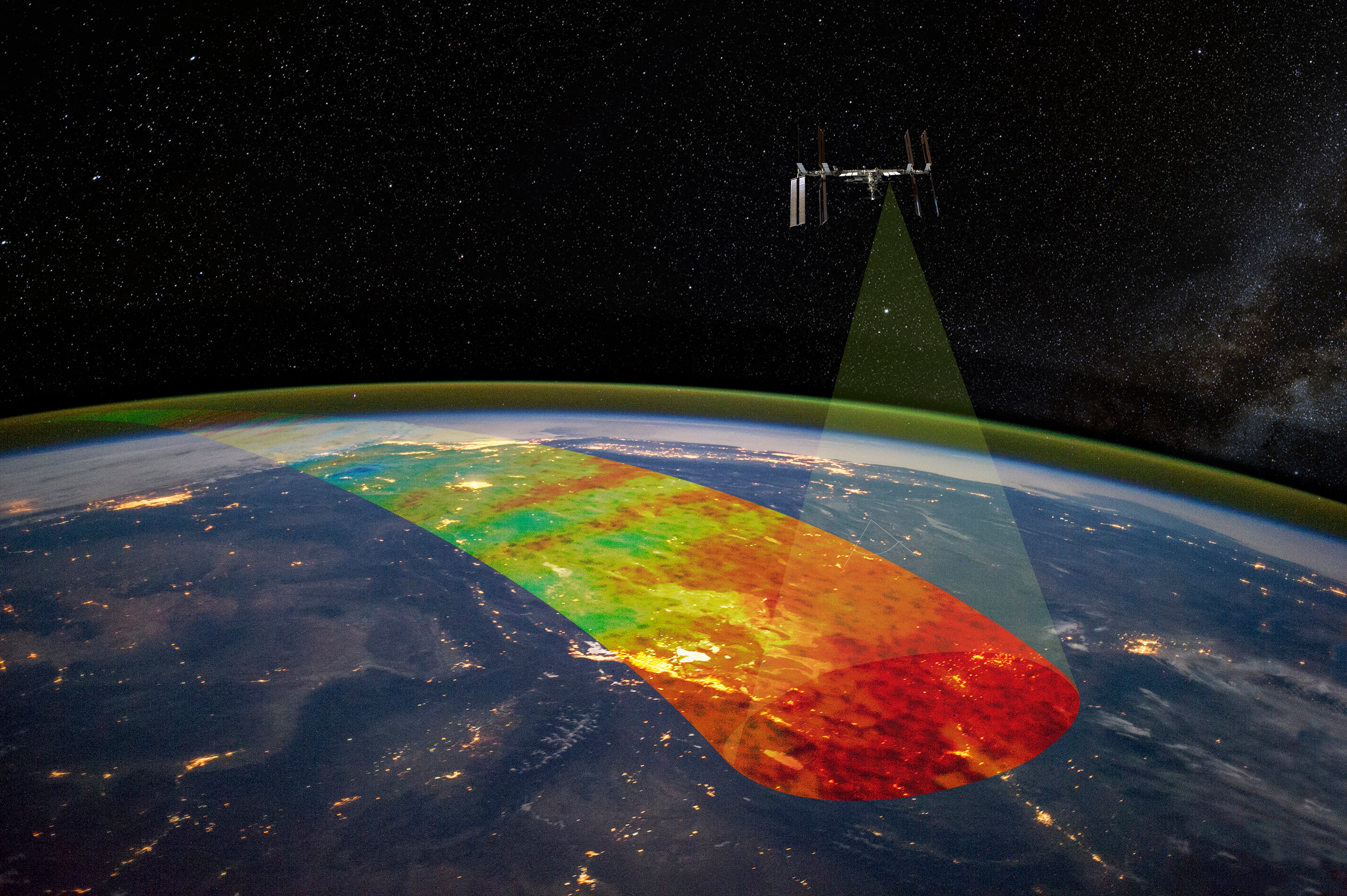 Above Earth, the International Space Station orbits. From one area toward the middle of the station, a transparent cone highlights a rainbow stripe of Earth's atmosphere.