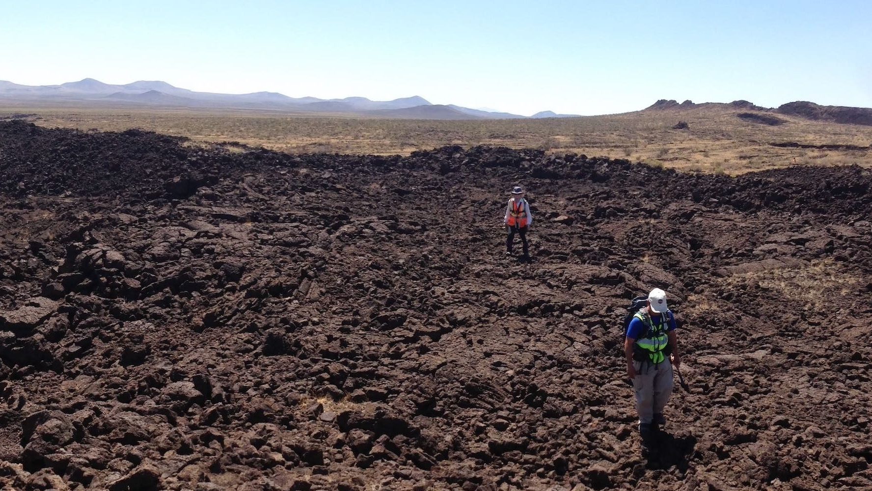 Scientists walk across lumpy, dark brown land