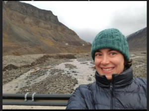 Elizabeth McDonald in a wool cap standing beside a mountain stream.