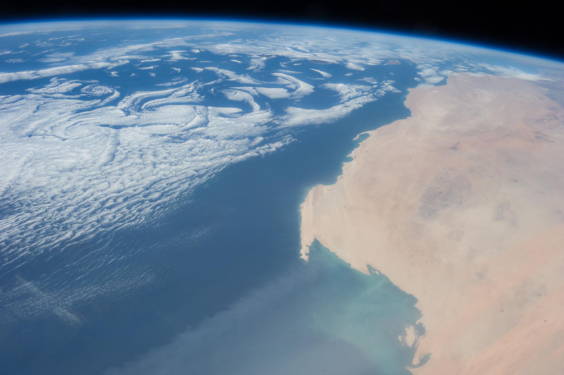 Satellite image of cloud formations over a blue body of water with land to the right.