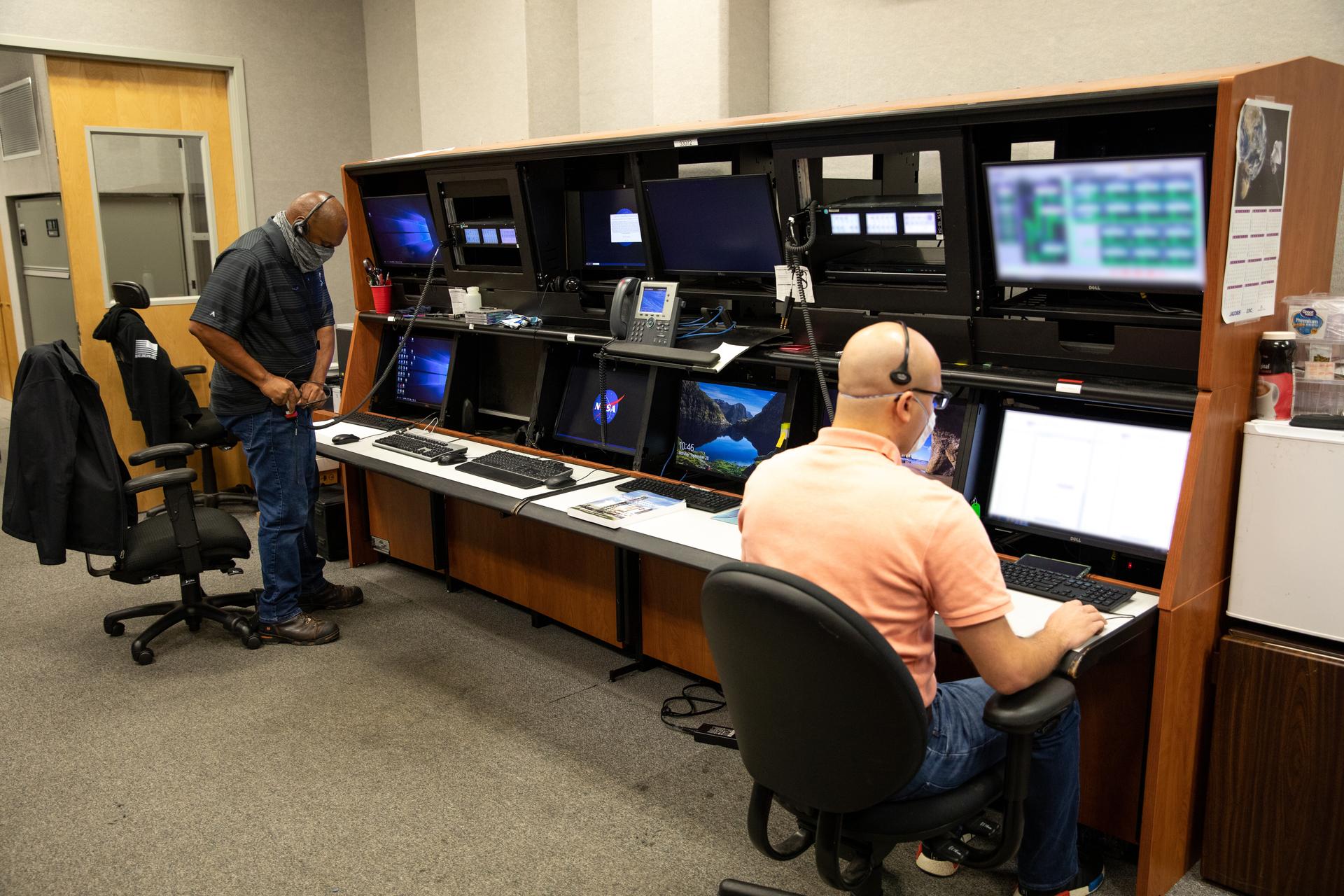 Two men wearing headsets and operating a bank of computers.