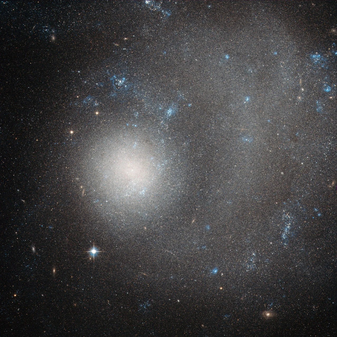 Hubble image of dwarf galaxy ngc 5474; a diffuse blob of stars off-centered with a vague swirl stretching right and up.