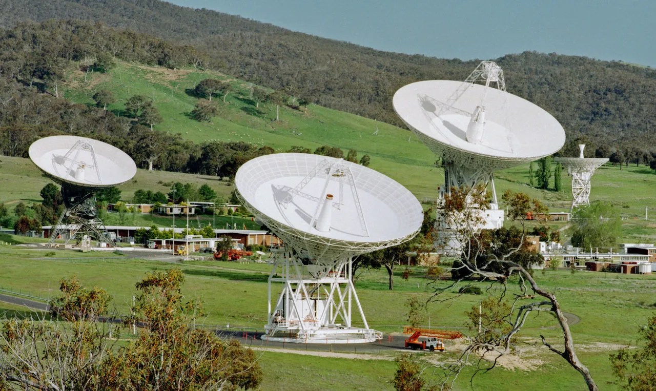 Large, white dish-shaped antennas on a green, grassy field.