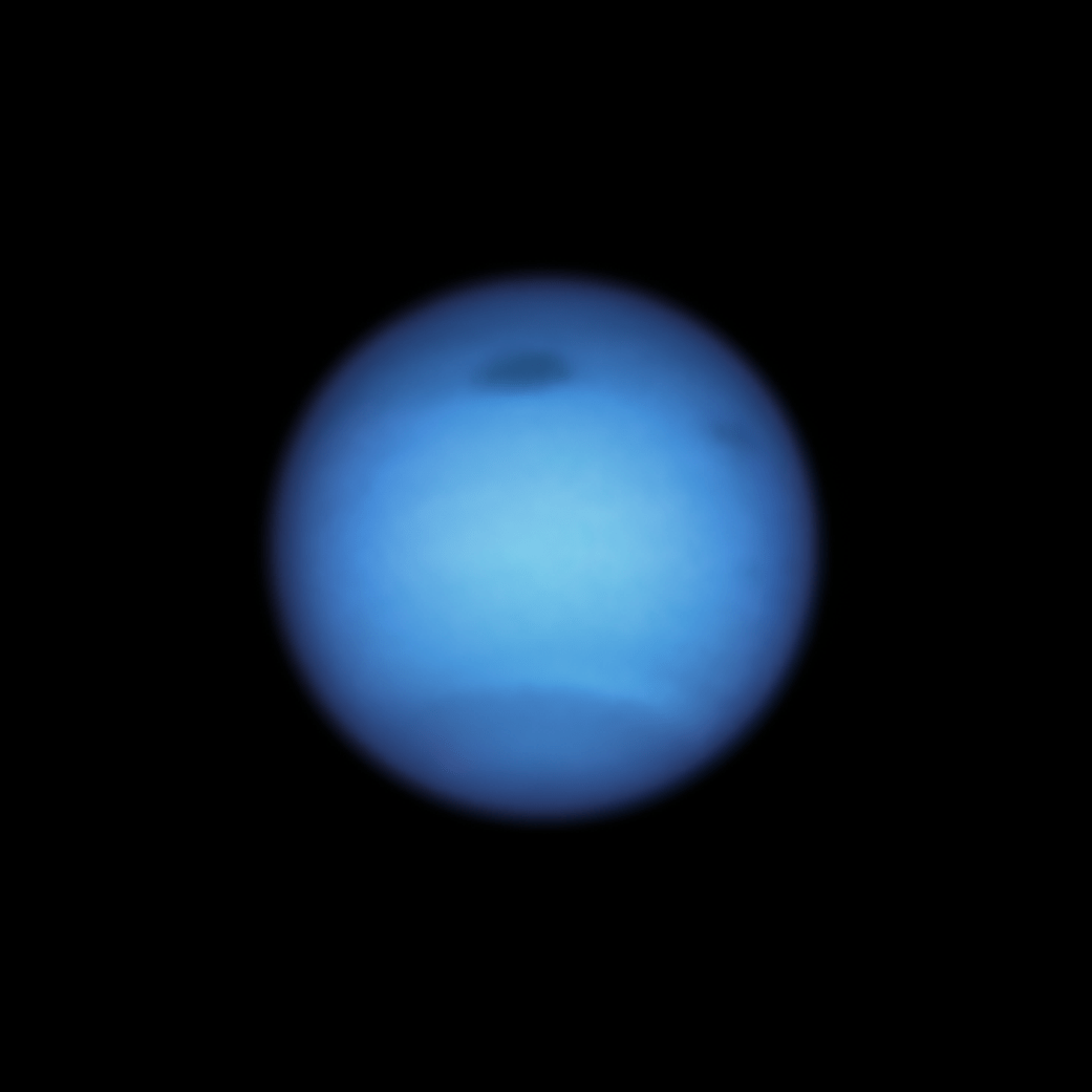 Sphere of Neptune seen. Dark blue circle with two small dark spots on the Northern portion.