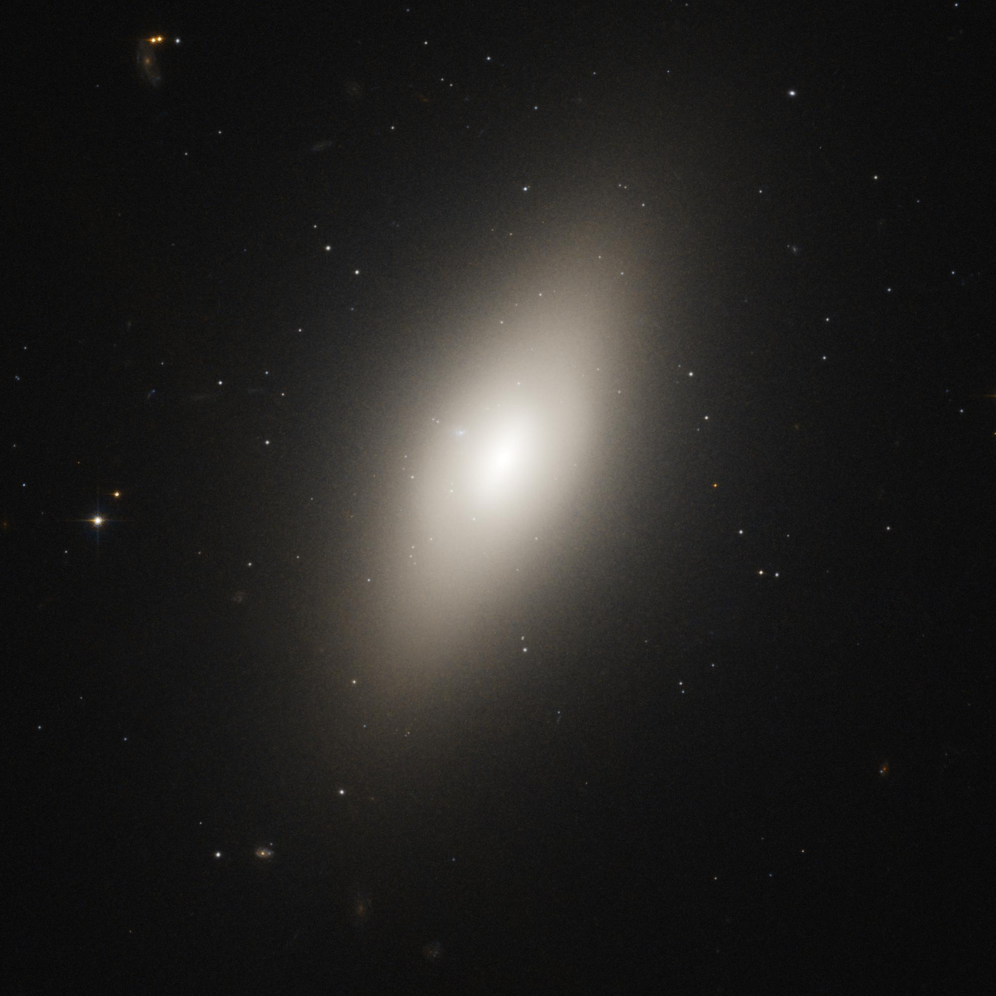 A bright-white elliptical galaxy extends from the lower-left to the upper-right of the image. Its core is at image center and shines bright-white.