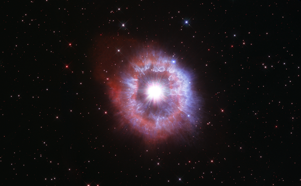 Bright-white star surrounded by a pinkish and white shell of gas. Black background dotted with stars.