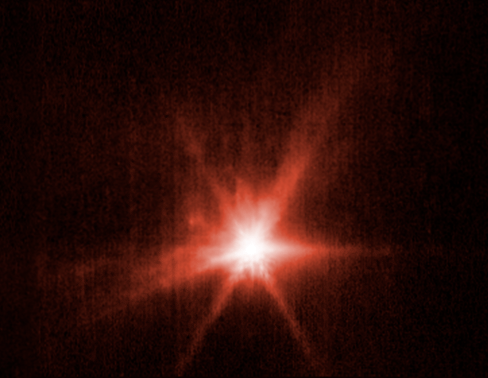 View of Didymos-Dimorphos asteroid system after DART impact. Webb's view, hued in red, shows a bright center and darker streaks emanating outward from it.