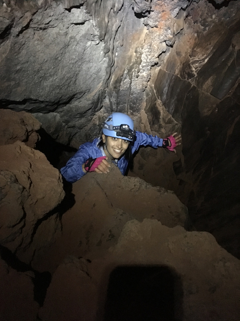 A scientist wearing a blue helmet with a light on smiles as they climb around rocks.