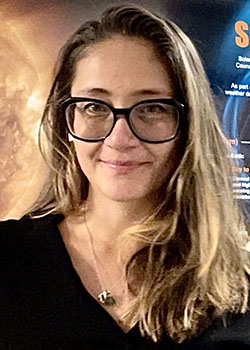 Portrait photo of a smiling woman with large glass frames and long hair.