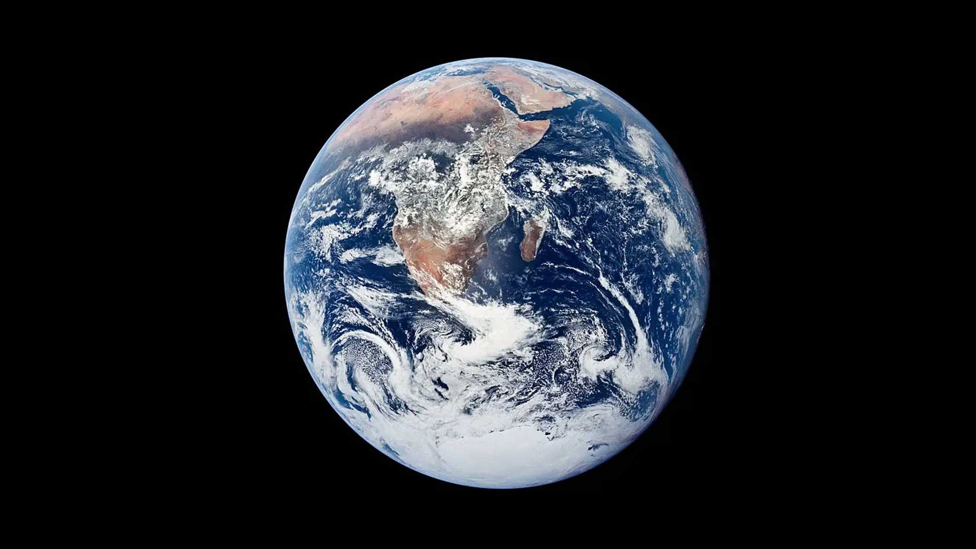 A view of Earth from Apollo 17 showing the blue ocean, reddish brown landmasses, and wispy, white clouds.