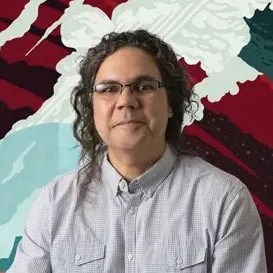 A Hispanic man sits smiling in front of a darkly colored poster for Enceladus, a moon of Saturn.