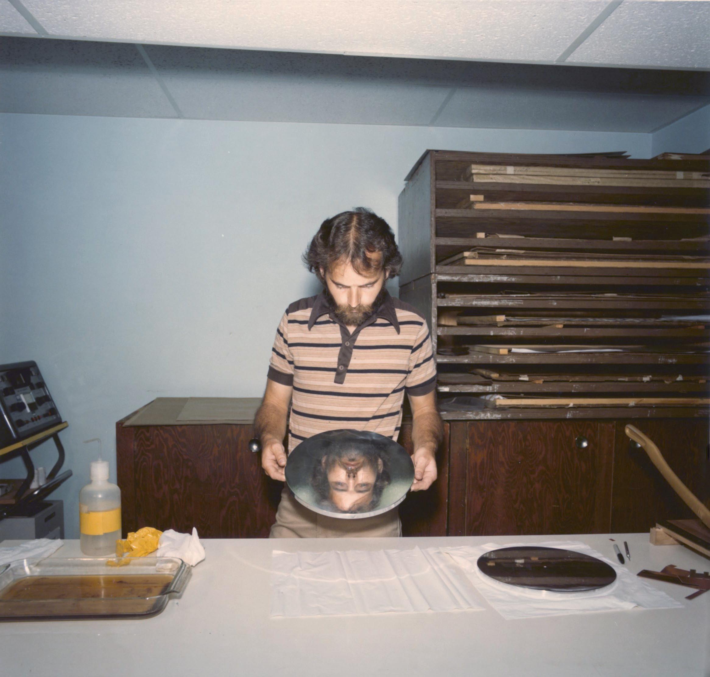 A man's face is reflected in a album-sized disc.