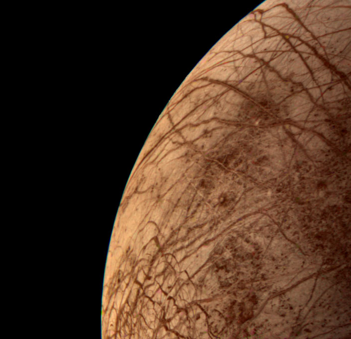 A partial view of Europa from Voyager 2. The moon looks red with darker read lines running across the surface.