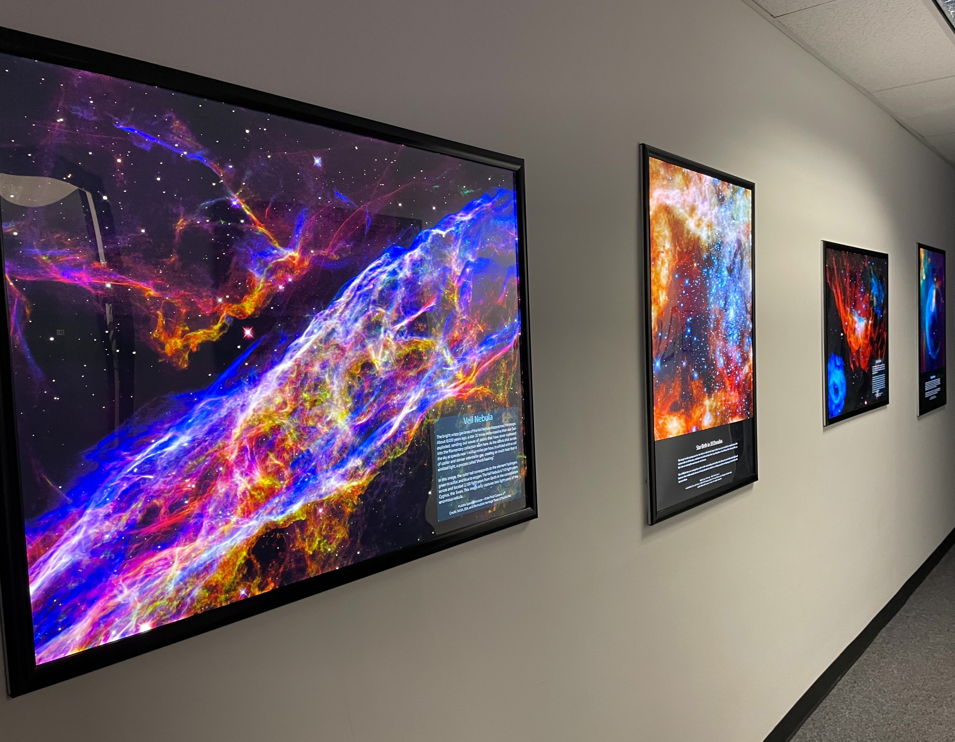 Framed colorful lighted galaxy images hanging along a tan wall.