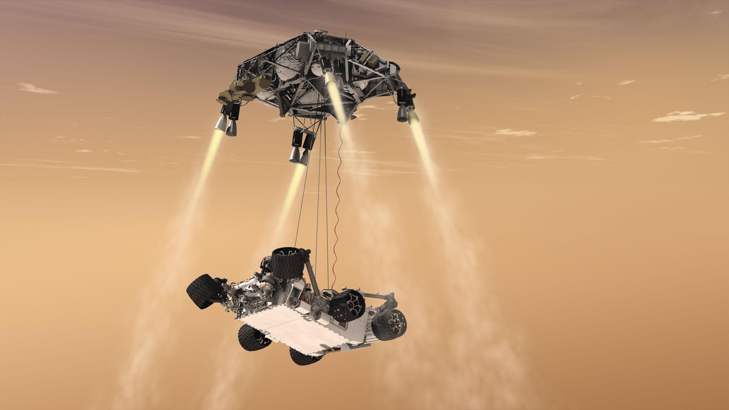 An illustration set against a pale orange sky shows a coaster-shaped spacecraft hovering at the top of the frame, with rockets at four corners firing jets toward the ground. Suspended beneath it on three tethers is a Mars rover, with a light-colored flat bottom, and its six wheels retracted above its belly.