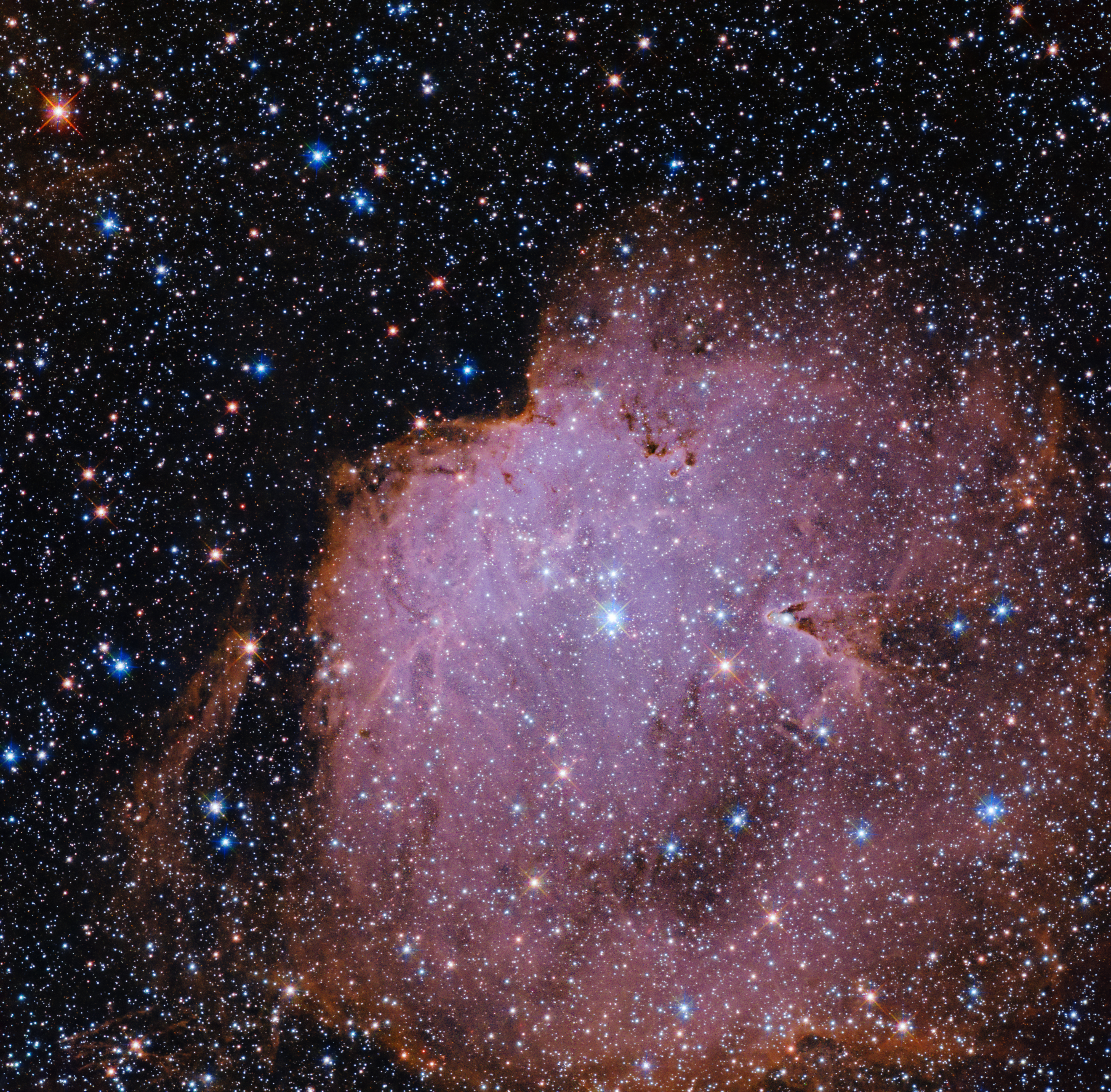 Thousands of stars fill the image against black space, with a glowing, nebulous cloud of pink dominating most of the lower right half of the view.