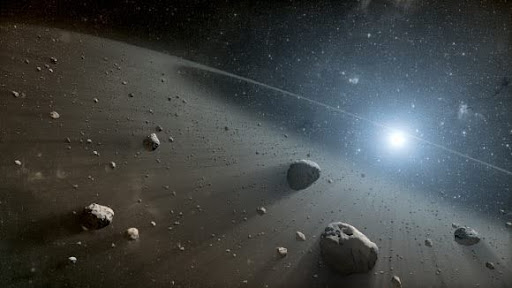 This is an artist’s concept of exoasteroids in space, featuring rocky asteroids of various sizes orbiting around a distant star. The scene depicts a dense asteroid belt, illuminated by the bright light of a star in the background, with dust and debris scattered throughout the space between the asteroids.