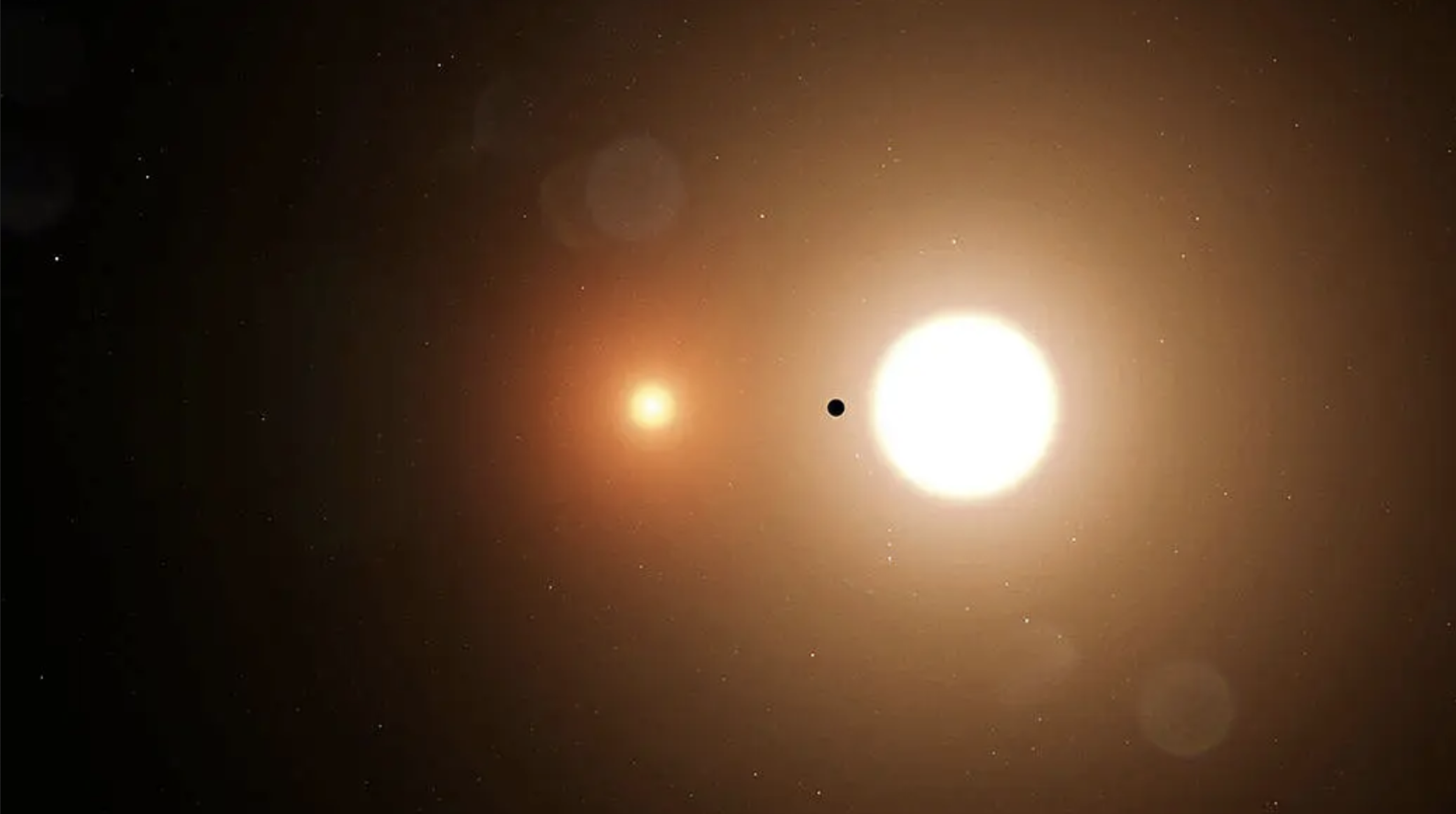 An image of a celestial scene showing two bright stars against a dark background, with one star appearing larger and more luminous on the right, and a smaller, dimmer star to the left. A planet is silhouetted as it transits in front of the larger star. The background is filled with a soft glow and scattered faint stars.