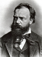 Portrait photographique noir et blanc d'un homme, fortement barbu, les cheveux décoiffés et portant un costume sombre et un foulard noué autour du cou.