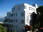 A white and silver building built with curved corners and streamlined features, stepped back along the slope of a hill.