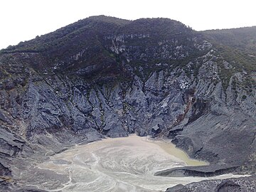 A photograph depicting a white sky at the top, a grey land configuration in the middle, and a body of water swirling around at the bottom.