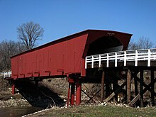 Photographie du Roseman Bridge à Madison. Le pont couvert est de couleur rouge marron, avec des barrières blanches qui le poursuivent