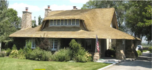 A country cottage with wrap-over roofing, surrounded by green meadow in a mountain town.