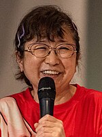 Mayumi Tanaka holding a microphone and smiling