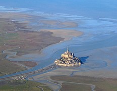 Vue aérienne du mont Saint-Michel : le rocher (sans les bâtiments) présente une base grossièrement elliptique de 950 m de circonférence pour une superficie de 28 ha, et mesure 91 m de haut[6].