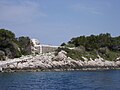 paysage d'île ; dans la végétation se devine un parallélépipède de marbre blanc au sommet d'une pente aménagée