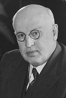 A bald man in a suit with round spectacles