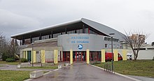 Vue d'un bâtiment moderne gris par temps couvert. Sur la façade, on lit « Patinoire de Colmar »