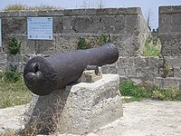 19th-century cannon, set in the wall of Acre near a sign commemorating Farhi. The Hebrew inscription on the sign reads: "Farhi vs. Napoleon. Jezzar's right hand in resisting Napoleon's harsh siege was the Jewish Haim Farhi, senior adviser and minister of finance"