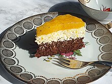 A slice of Fanta cake served on a plate. It is a three-layered sponge cake, where the top layer is made out of Fanta.