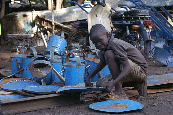 Blacksmith/recyclers of Médine district in Bamako, Mali: Boy beating old sheet metal flat for the recycling of scrap metal into watering cans