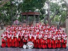 Large group of musicians in red clown costumes, in front of a gazebo