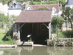 Photographie en couleurs d'un bâtiment ouvert muni d'une planche à laver au bord d'une rivière.