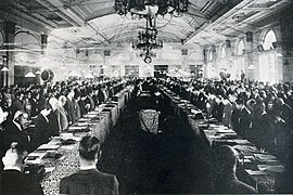 photo d'une grande salle de réception. Deux rangées de tables et les convives d'un banquet sont visibles.