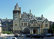 Photographie en couleur d'un château de style néogothique devant lequel sont garées de nombreuses voitures.