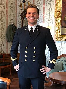 A Caucasian man with dark hair posing in a navy uniform in an old room