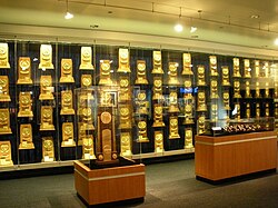 A room with glass display cases containing rectangular, wooden trophies that are gold-plated.