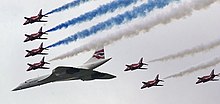 BA-liveried Concorde leading a V-formation with seven of the Red Arrow's Gnat aircraft in view. The Gnats are trailing blue and white smoke