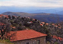 View of a valley with many stone houses along the hill. These are small with red brick roofs.