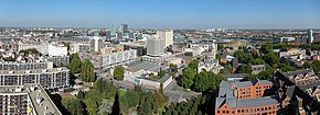 Photographie en couleur proposant une vue surplombante de la ville avec au premier plan, le quartier Saint-Sauveur et ses immeubles des années 1950 à 1970, au deuxième plan, les bâtiments modernes d'Euralille, et, au fond, la silhouette de quelques bâtiments de Villeneuve-d'Ascq