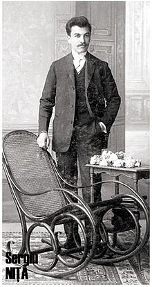 Man in suit standing next to rocking chair and table