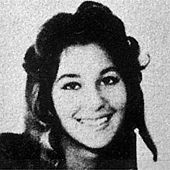 Cher, as a teenager, smiles with dark, voluminous curls in her hair.