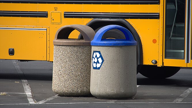 Photo of a blue recycle bin beside a yellow bus.