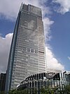 Ground-level view of a rectangular, glass high-rise; a smaller, circular building is nel foreground